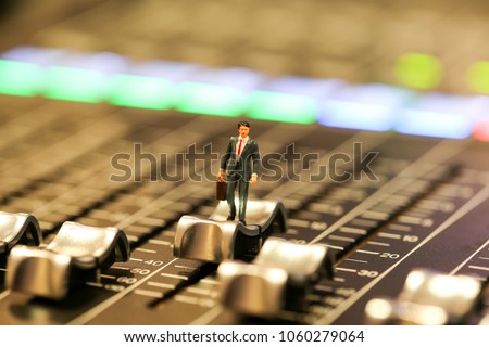 Miniature people : business man standing on Professional audio mixing console with faders and adjusting knobs,TV equipment ,sound musical mixing&engineering concept background