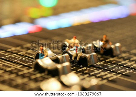 Miniature people : business man sitting on Professional audio mixing console with faders and adjusting knobs,TV equipment ,sound musical mixing & engineering concept background