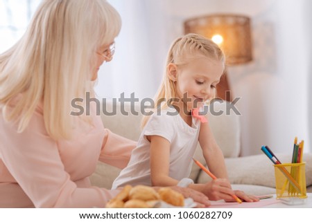 Creative child. Positive joyful happy girl smiling and holding a pencil while drawing a picture