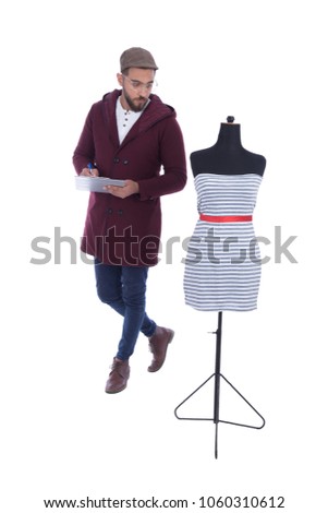 Full-length shot of a handsome young man wearing winter outfit sitting on a stair, looking at the dress that his designing and writing his thoughts, isolated on white background