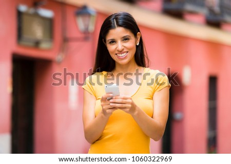 Happy young latin woman talking and texting on smart phone, wearing casual clothes sitting in with a take away coffee in a urban bench  Royalty-Free Stock Photo #1060322969
