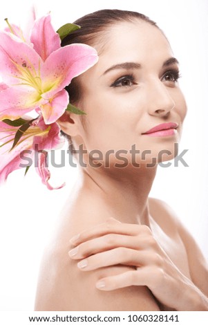 Portrait shot of pretty young woman with pink lily flowers in her hair looking away while posing for photography against white background