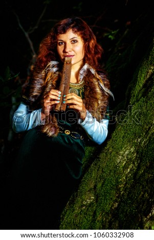 girl in historic dress with wooden flute in woodland country with bemoosed rocks.