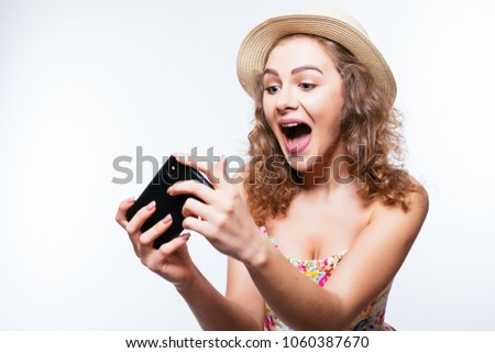 Cheerful excited girl in cap play games or make video call on smartphone on white background
