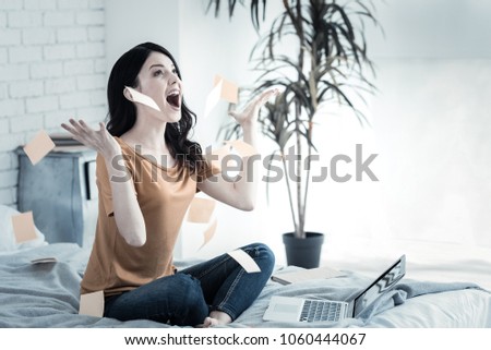Stressed out. Pleasant emotional young woman sitting in front of the laptop screen and throwing pieces of paper while being stressed out