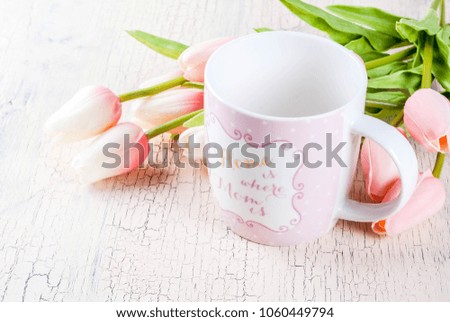 Mother's Day concept, greeting card background. Flowers tulips on a light concrete table, mug with inscription "Home is where the mom is", greeting note Happy Mother's Day copy space