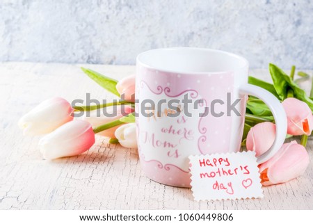 Mother's Day concept, greeting card background. Flowers tulips on a light concrete table, mug with inscription "Home is where the mom is", greeting note Happy Mother's Day copy space