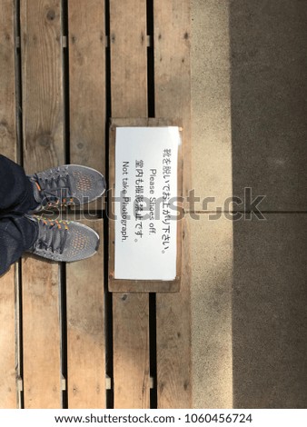 Man's feet stand on wooden floor with sign of "please take shoes off" and "Not to take photograph" before proceeding into the area
