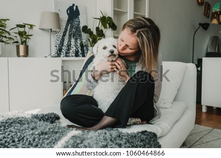 Young and beautiful sweedish blonde girl playing with her cute little french bichon dog at home. Sweet relation. Lifestyle photography