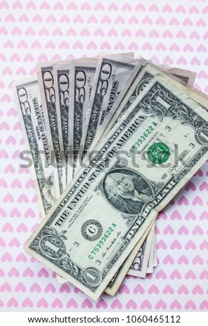 Money is lying on the background with pink hearts. Loving dollars. Time to go shopping and buy things. Money addicted shopaholic. Vertical photo.