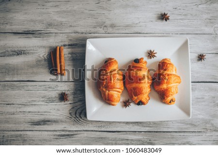 coffee with croissants in a white dish sprinkled with cinnamon and anise on a light wooden table