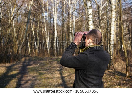Young man looks through binoculars in search of birds, bird watching