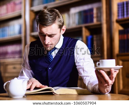 Five oclock tea tradition concept. Young man with antique bookshelves on background. British elite or aristocrats spend leisure in library. Intelligent, man in suit with good manners hold cup of tea.