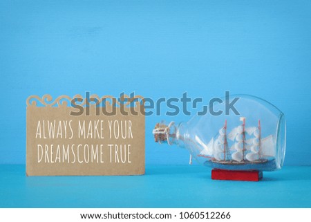 nautical concept image with sail boat in the bottle and note over blue wooden table
