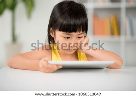 Portrait shot of cute Asian girl watching educational program on digital tablet while spending weekend at home, blurred background