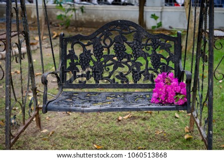 black iron classic outdoor hanging patio porch swing bench in the garden. Decorative aegean and Bougainvillea flower begonia
