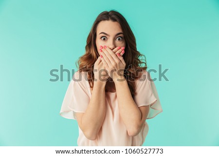 Portrait of a shocked young girl in dress looking at camera with mouth covered isolated over blue background Royalty-Free Stock Photo #1060527773