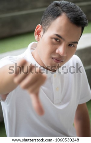 rejecting man showing thumb down gesture; man denying with thumb down, concept of deny, rejection, turn down, negative feedback, bad, no; asian young adult man model
