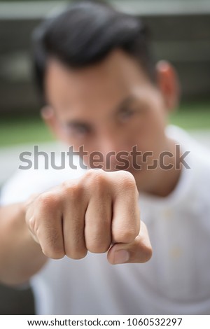man punching; strong man clenching his fist portrait; man fighter in fist fighting pose looking at you; asian young adult man model