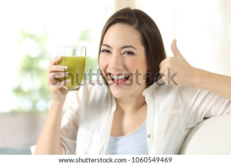 Woman holding a vegetable juice with thumbs up sitting on a couch in the living room at home