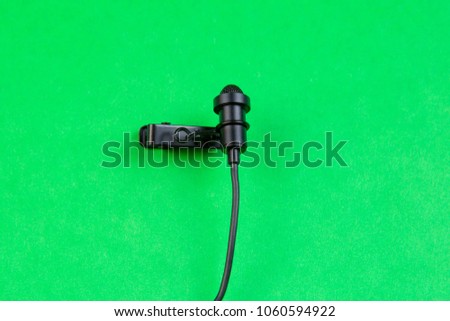 Miniature microphone of the buttonhole. A small microphone for recording quality sound on a green background. Lavalier microphone