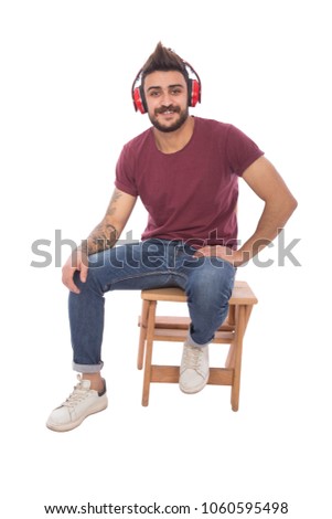Handsome young man wearing a casual outfit, sitting on wood stairs, putting his earphone listening to music, isolated on white background