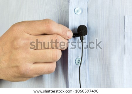 A small buttonhole microphone on a man's shirt. The man fixed the mini microphone to his blue shirt. Lavalier microphone