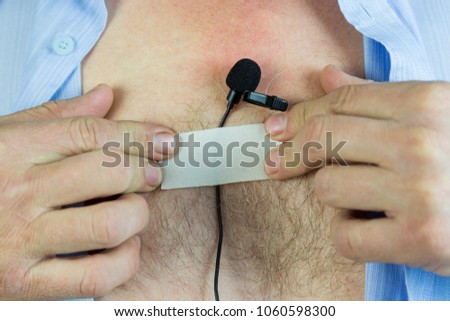 Lavalier microphoneA man attaches a hidden microphone to his chest with an adhesive tape. A private detective puts on a small microphone a buttonhole under his shirt for secret recording of the sound.