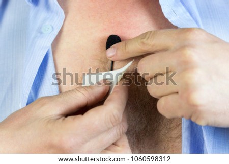 A man attaches a hidden microphone to his chest with an adhesive tape. A private detective puts on a small microphone a buttonhole under his shirt for secret recording of the sound. Lavalier microphon