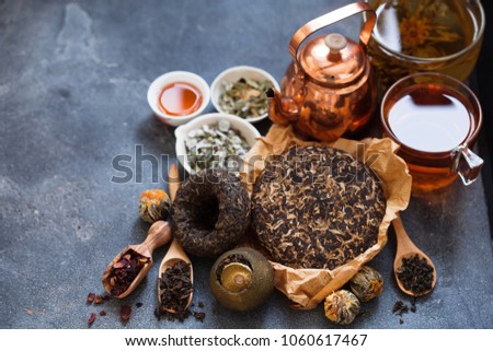 Different sorts of tea; Asian pressed pu-erh tea, shu pu'er in tangerine, blooming tea in ball, hibiscus, herbal on dark slate background 