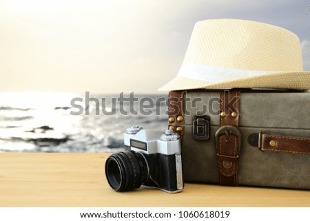 traveler vintage luggage, camera and fedora hat over wooden table infront of sunset landscape. holiday and vacation concept.