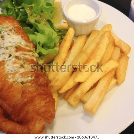 Fried fish steak served with french fries and vegetables on white dish