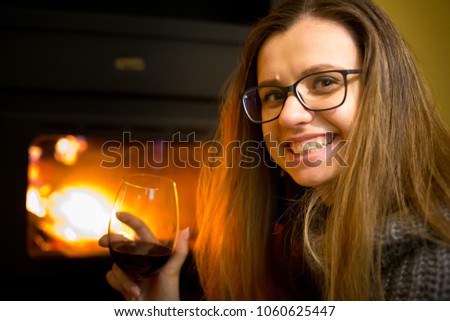 Beautiful girl sitting on the floor in a warm room next to a fireplace with a glass of wine in hand