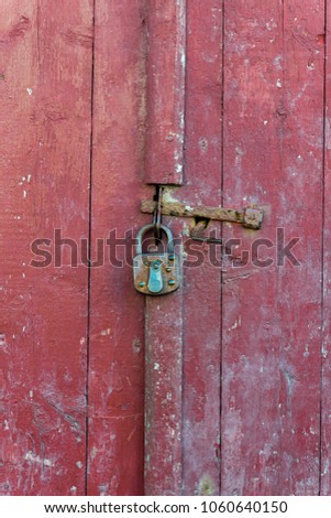 An antique lock and latch on an old vintage red wooden door. The padlock and latch is 
very rusty.