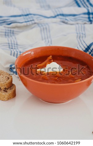 Traditional Ukrainian Russian vegetable borscht with sour cream, bread, kitchen towel in red bowl.