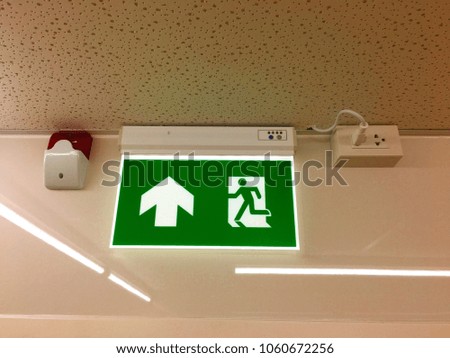 Green sign of fire escape with daylight lamp on white wall at stores