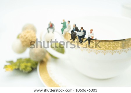 Miniature people: Business man sitting, waiting and reading newspaper or book on white gold cup of hot coffee at coffee shop using as background business concept.