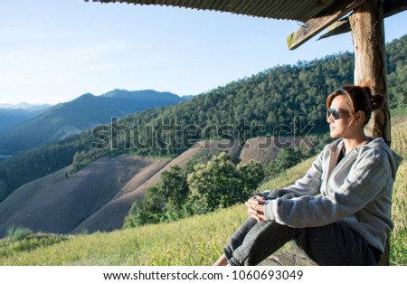 Picture of attractive Asian women sitting in a cottage with landscape mountains green fields and corn farm in the morning