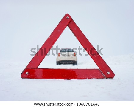 Winter road, snowstorm, heavy snow. Forced stop. Warning red triangle. A broken car. Road accident. Request for help. Danger, there is no way forward. Blurred background. Snow-covered road. Loneliness