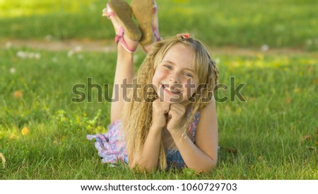 Beautiful young blonde girl lying on a field, green grass. Outdoors Enjoy Nature. Healthy Smiling Girl lying in Green Grass