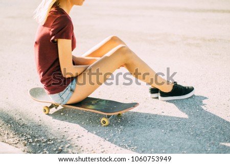 Young girl is sitting on a skateboard, tattoo on her leg