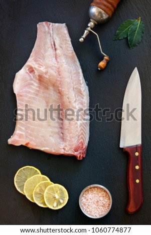 Close-up photo of fresh raw fish fillet with sea salt and lemon on black concreted table background