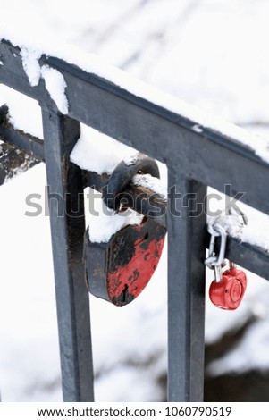 Two metal iron locks - big and small red, hang on a cast-iron fence in winter, covered with snow.