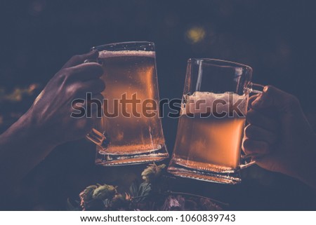 Two mugs of light beer in hands with hop against background of green park trees outdoor picnic, outing party rest on nature, vintage toning picture