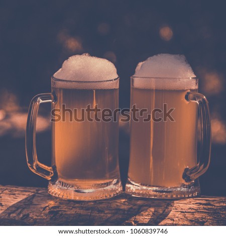 two beer with foam in mug on green outdoor background, vintage toning picture