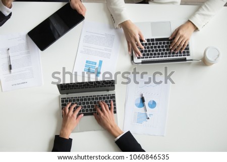 Top view of office workers typing at laptop, with smartphone and handouts around during board meeting. Marketing analysis financial team cooperating, discussing business ideas in coworking space. Royalty-Free Stock Photo #1060846535