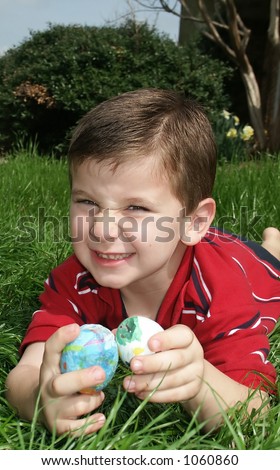 A young boy making a funny face and holding two Easter eggs.