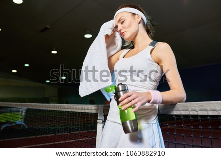 Waist up portrait of female tennis player wiping sweat with towel  taking break from practice in indoor court, copy space