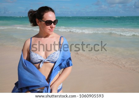 Smiling young adult Caucasian woman in sunglasses with blue pareo on the beach. Outdoor portrait