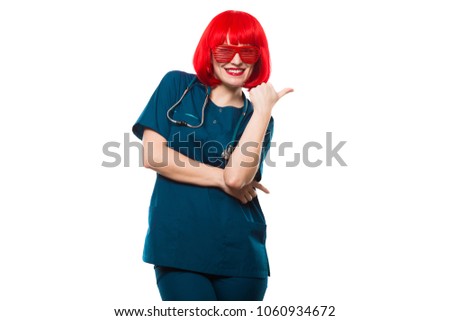 Attractive funny smilling caucasian brunette female doctor in red wig and red sunglasses standing in office having a break fooling